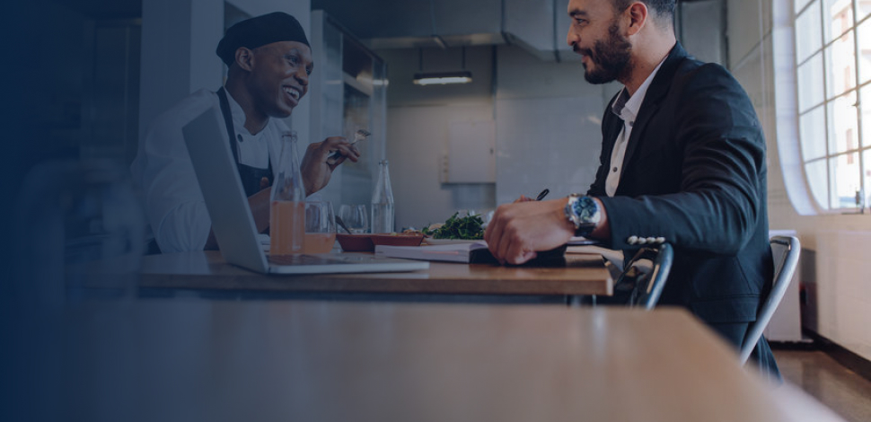 Smiling restaurant manager sitting at table and talking with chef