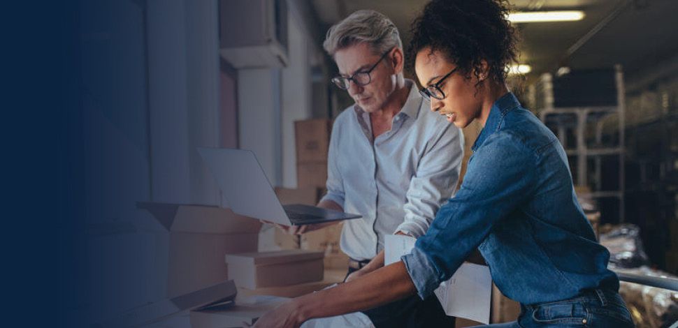 Woman packing the product in box with man working on laptop.