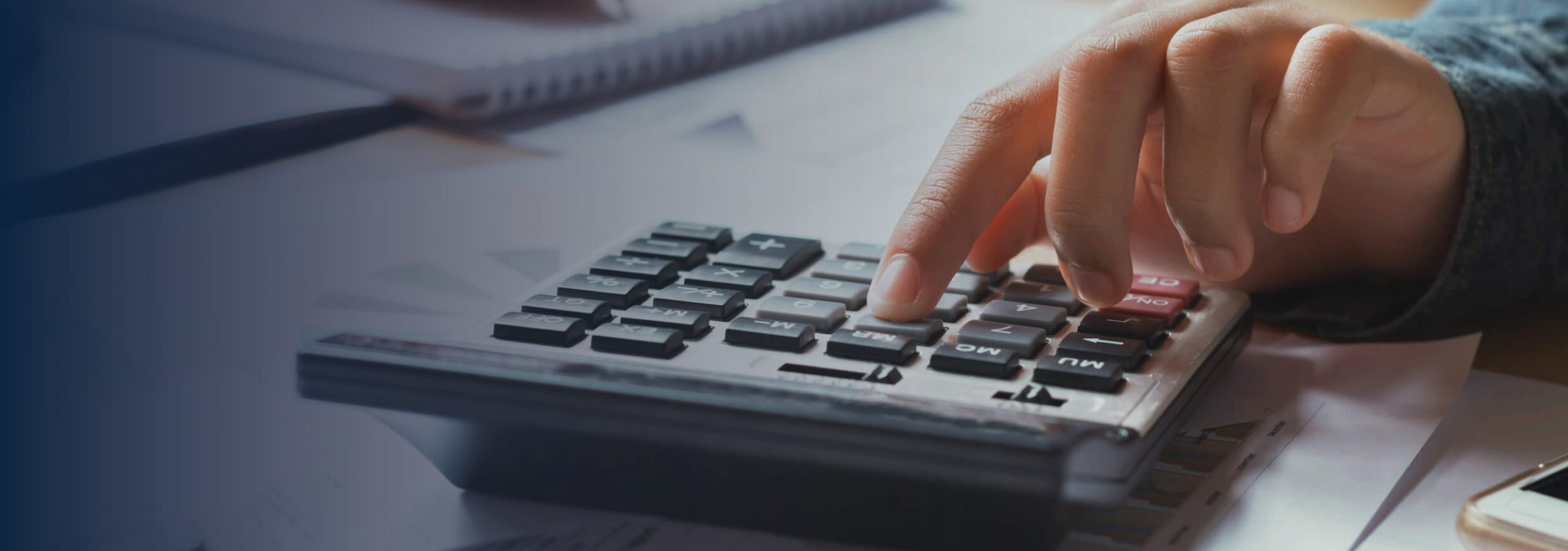 Hand using calculator with paperwork in the background