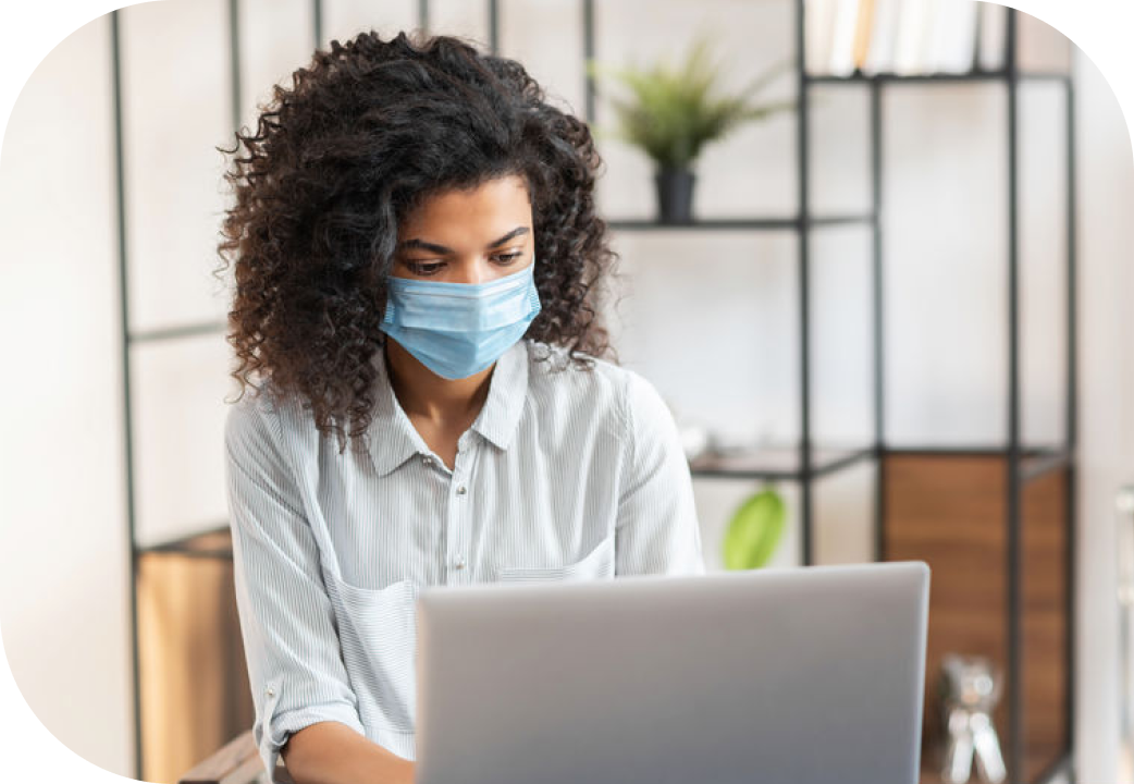Woman wearing a protective face mask sitting at the desk and working on a laptop