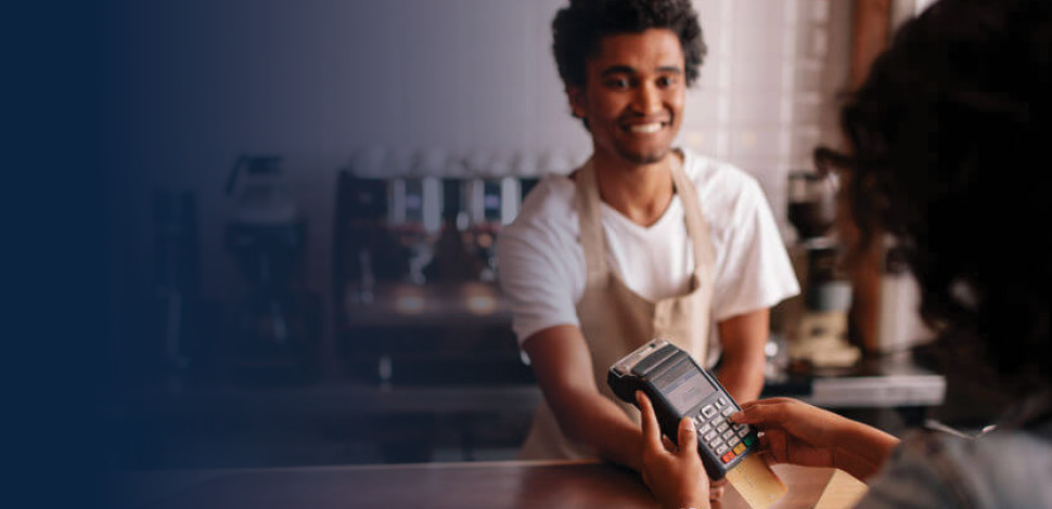 Male coffee shop employee passing a customer the payment terminal.