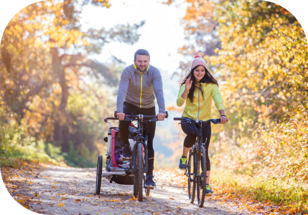 Young family with baby in jogging stroller cycling outside