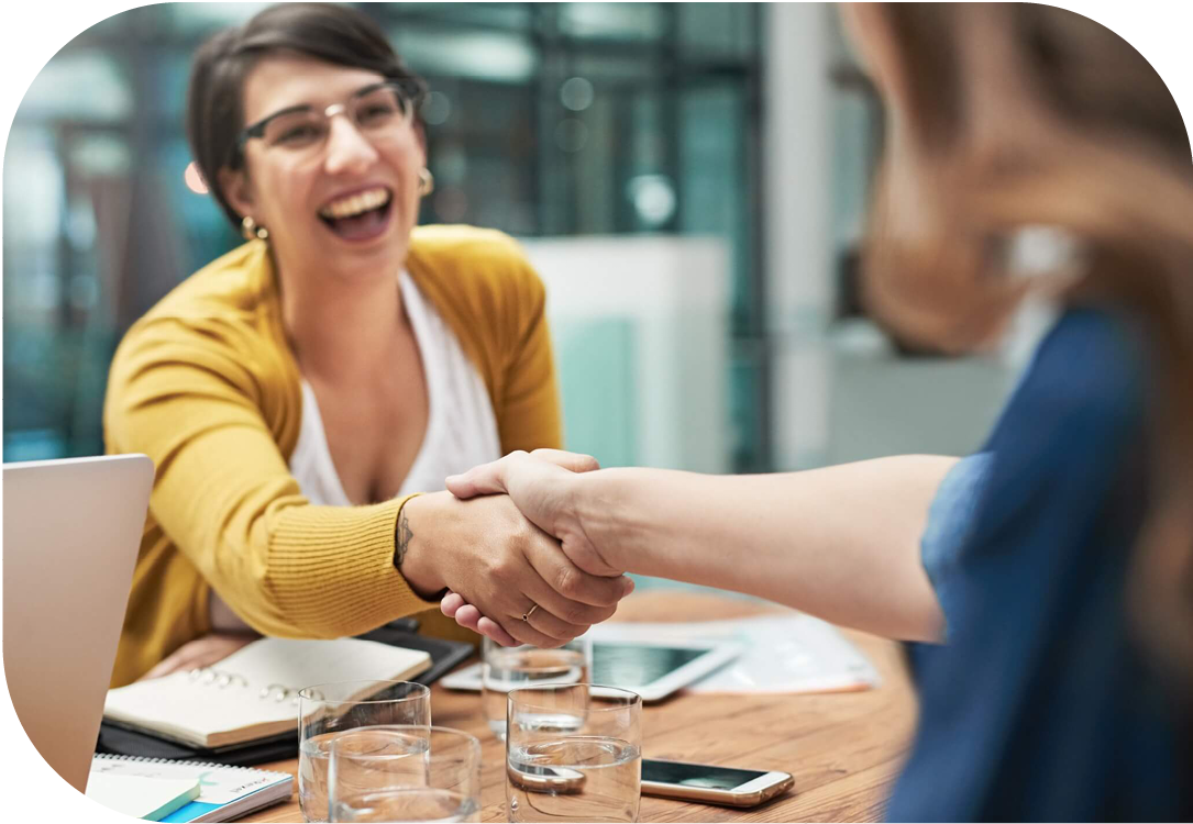 Two women shaking hands across a desk.