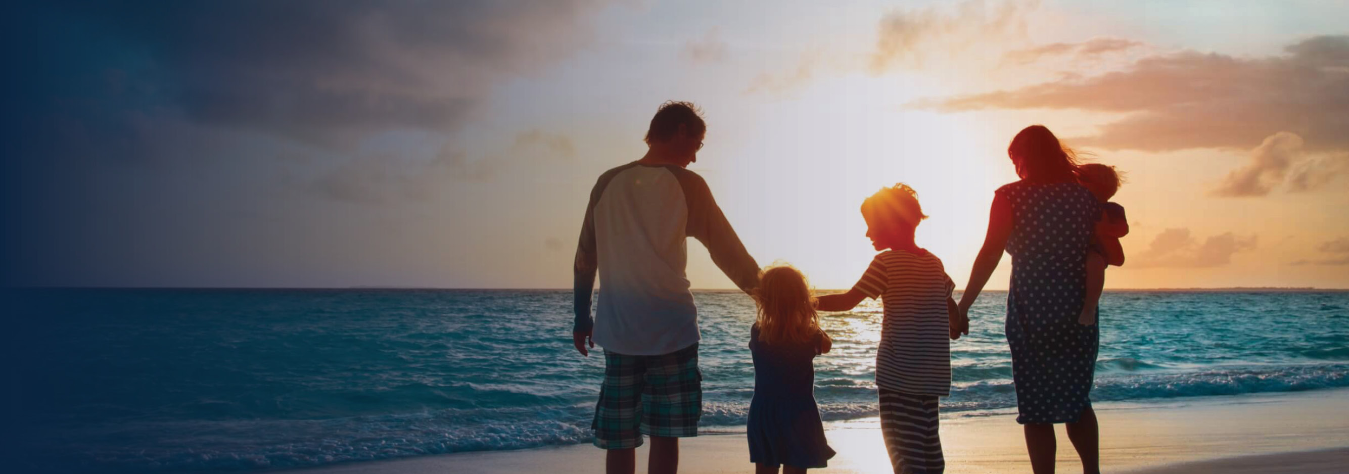 Family standing at the shoreline of the ocean at sunset.
