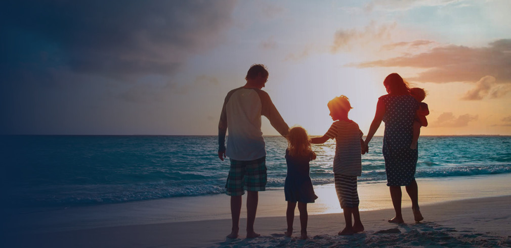 Family standing at the shoreline of the ocean at sunset.