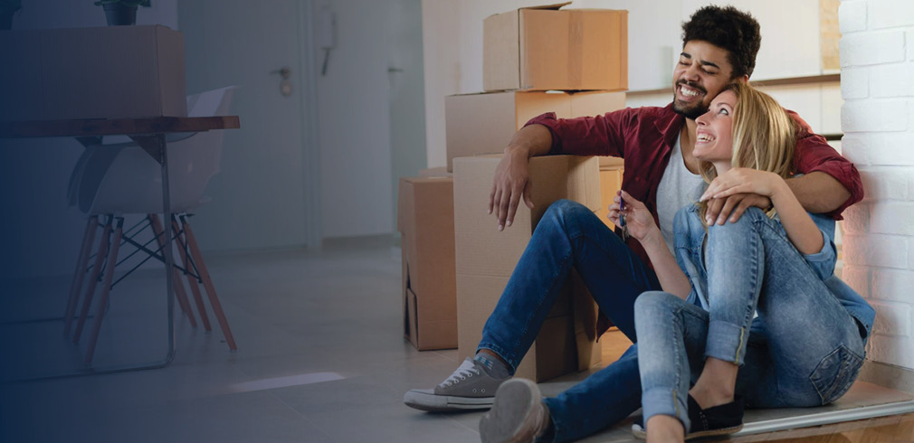 Couple sitting in new home surrounded by moving boxes.