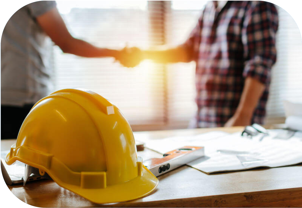 Two men shaking hands behind desk with house plans and hard hat.