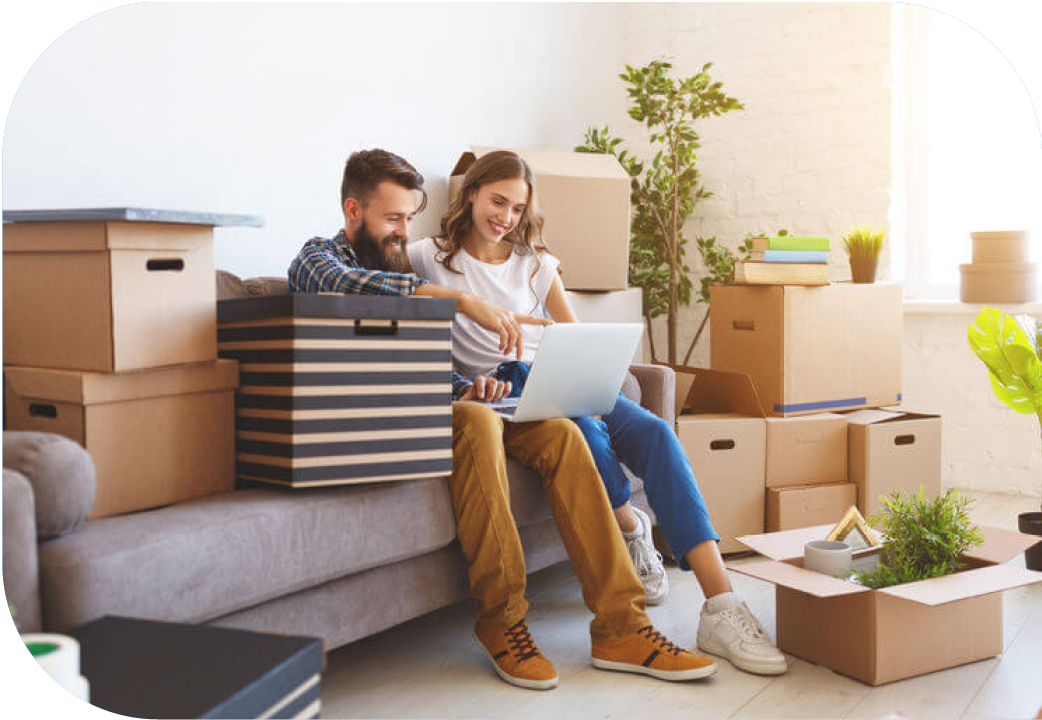 Young couple surrounded by moving boxes, looking at laptop.