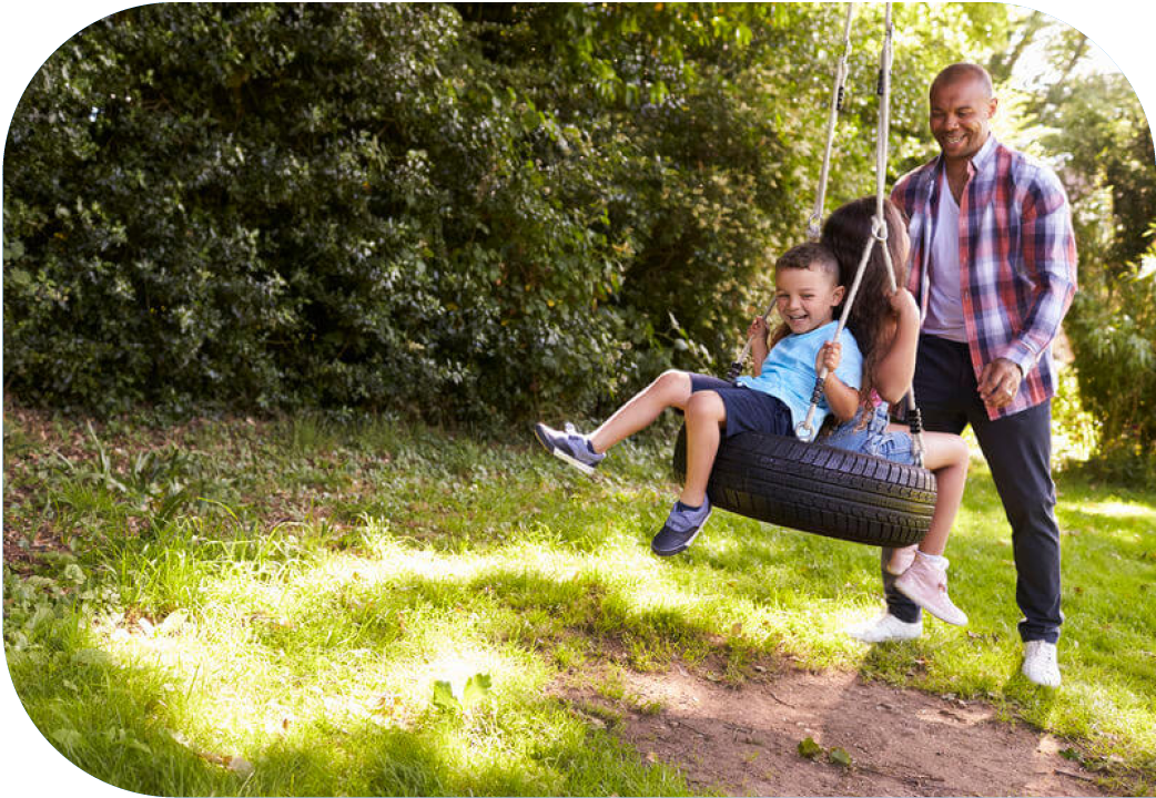 Dad pushing two young kids on a tire swing