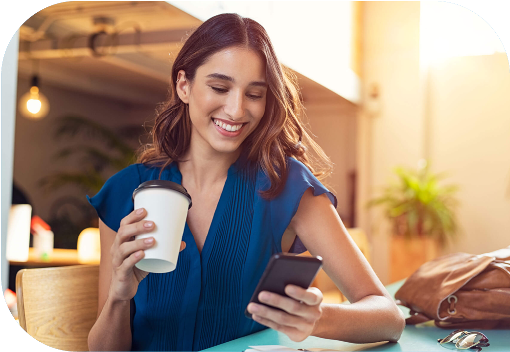 Woman sitting outside holding coffee while using her mobile phone