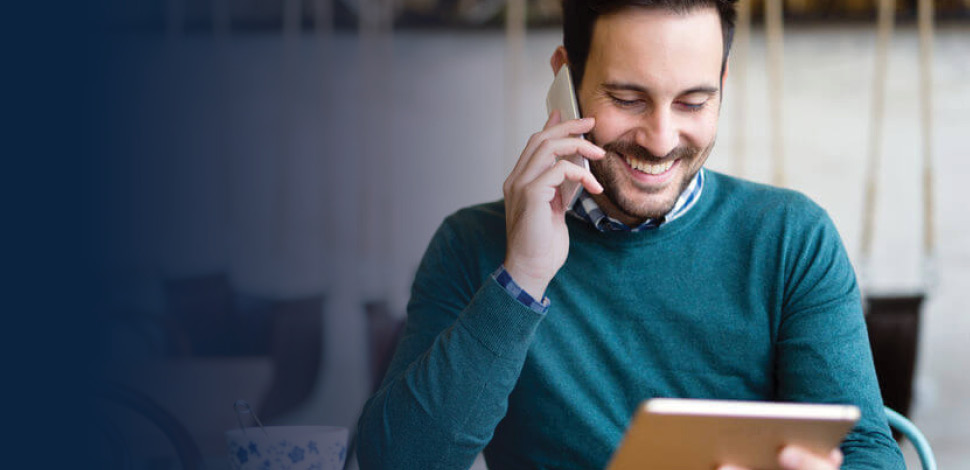 Man in cafe looking at tablet while talking on cell phone